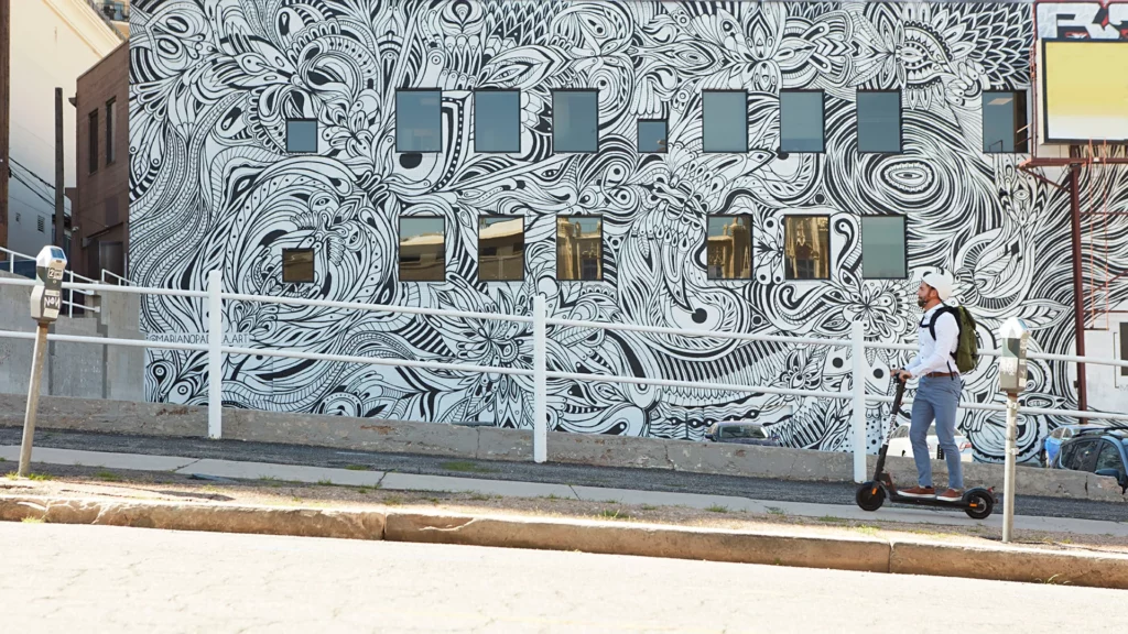 Egy férfi emelkedőn megy fel a GoTrax XR Ultra rollerével, egy gyönyörűen megfestett fal előtt