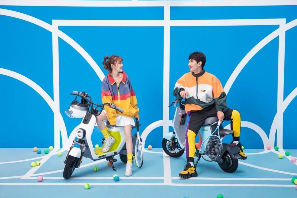 Két barát ül a Segway eMoped C80 mopeden egy berendezett helyiségben, aminek kék fala van